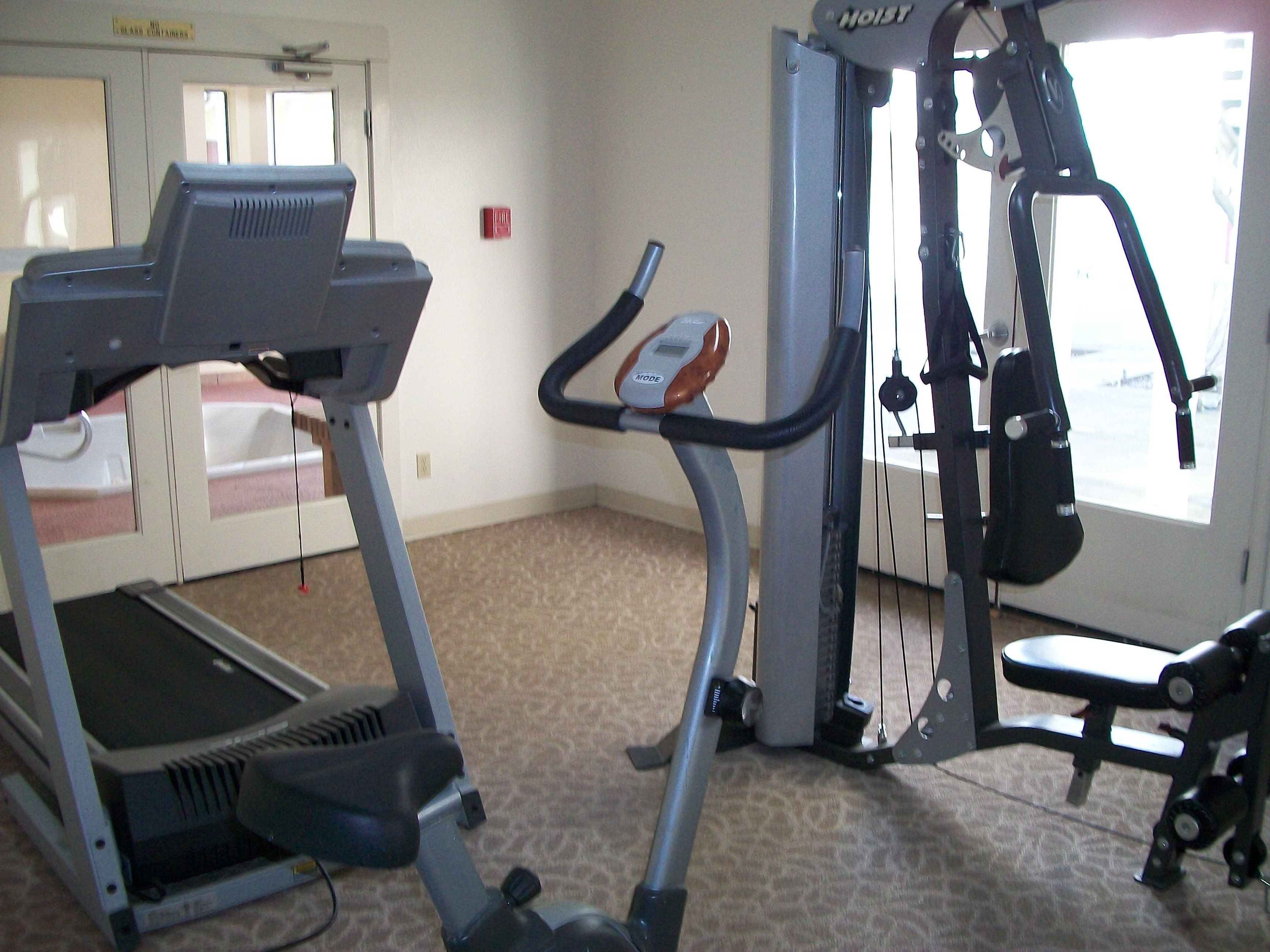 Une salle de sport équipée d’un tapis de course, d’un vélo elliptique et d’appareils de musculation.