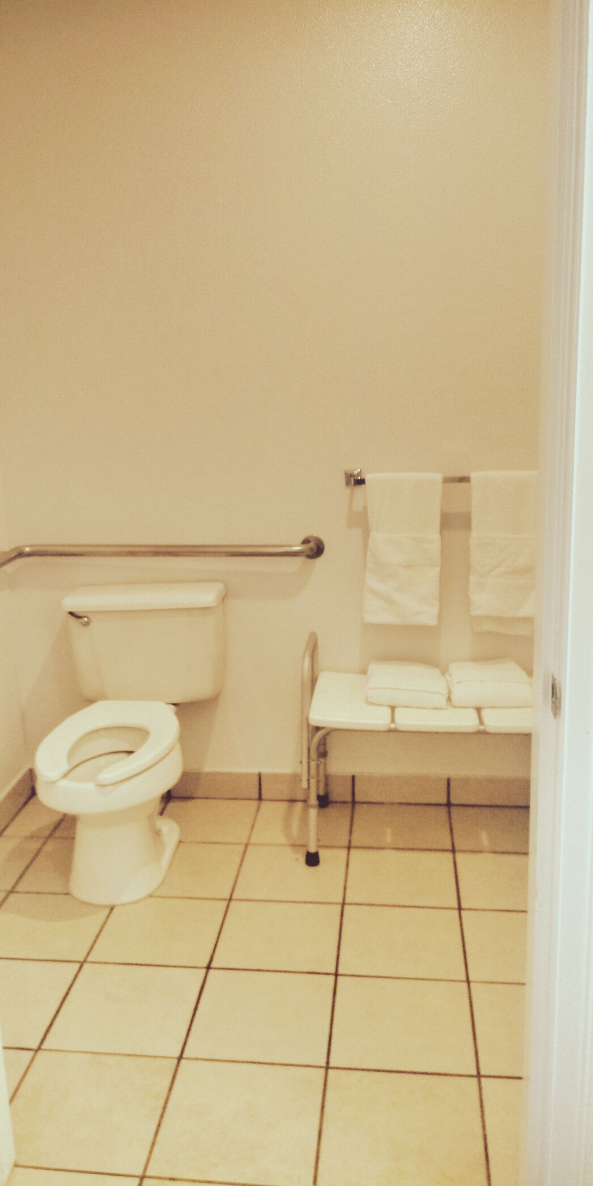 A bathroom with a toilet, a handrail, and a bench with towels.