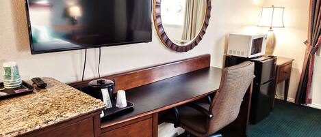 Habitación de hotel con televisión de pantalla plana, escritorio de madera, silla, microondas y lámpara.