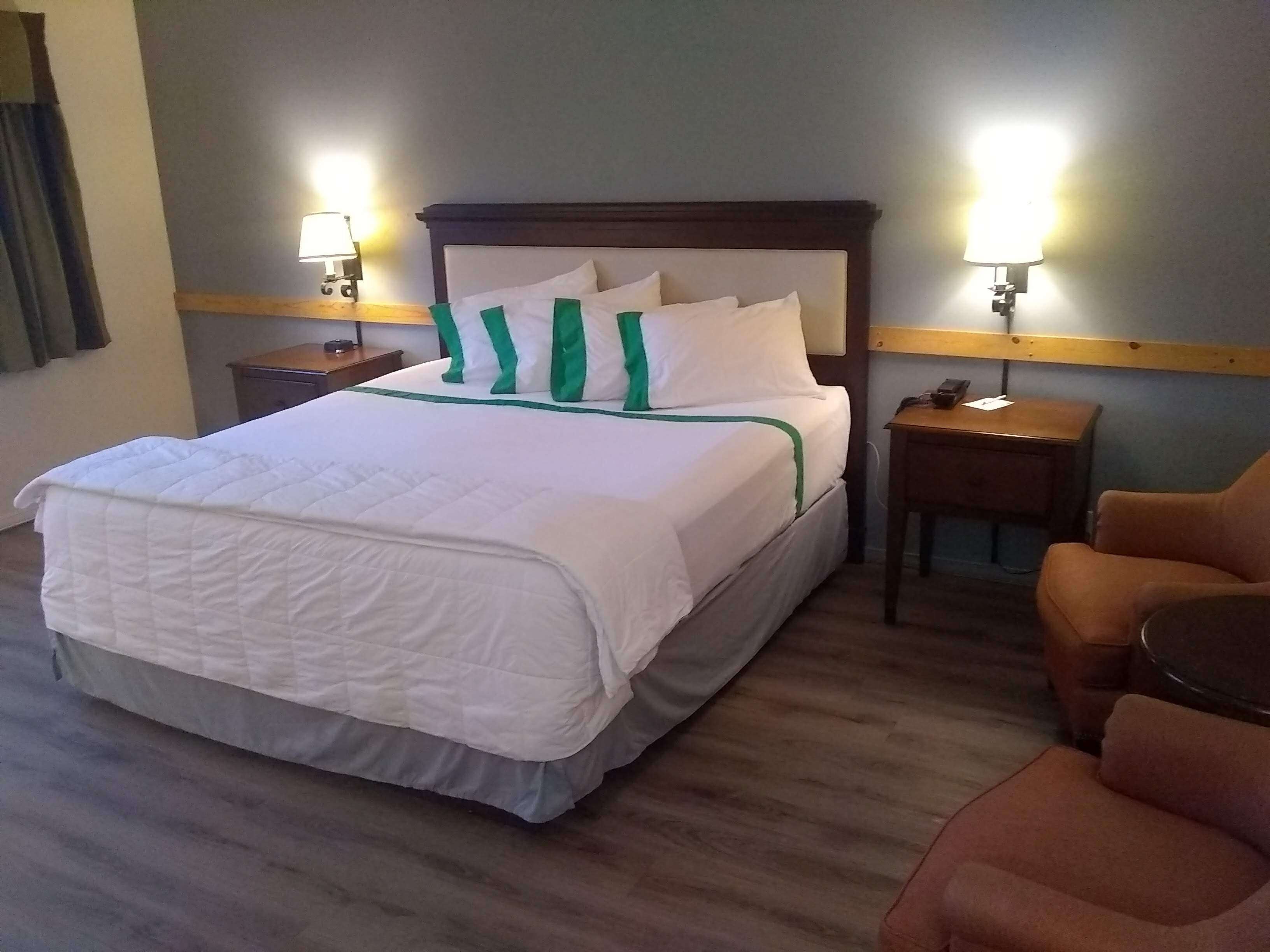 Hotellihuone, jossa on suuri sänky, kaksi yöpöytää, tuoli ja kaksi seinään kiinnitettyä lamppua.