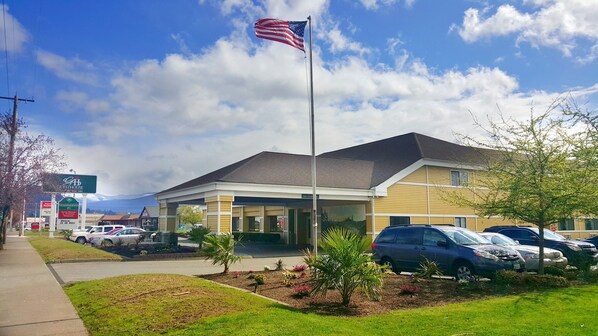A hotel with a flagpole, a parking lot, and a sign for a restaurant. - GuestHouse Enumclaw (Enumclaw)