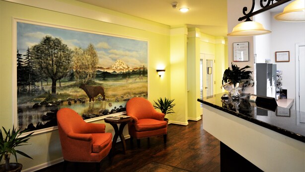 A lobby with a mural, two orange chairs, a reception desk, and a potted plant. - GuestHouse Enumclaw (Enumclaw)