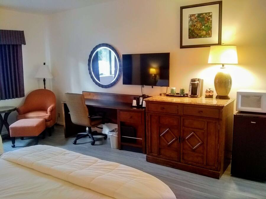 Quarto de hotel com cama, escrivaninha com cadeira, televisão, luminária, cafeteira e micro-ondas.