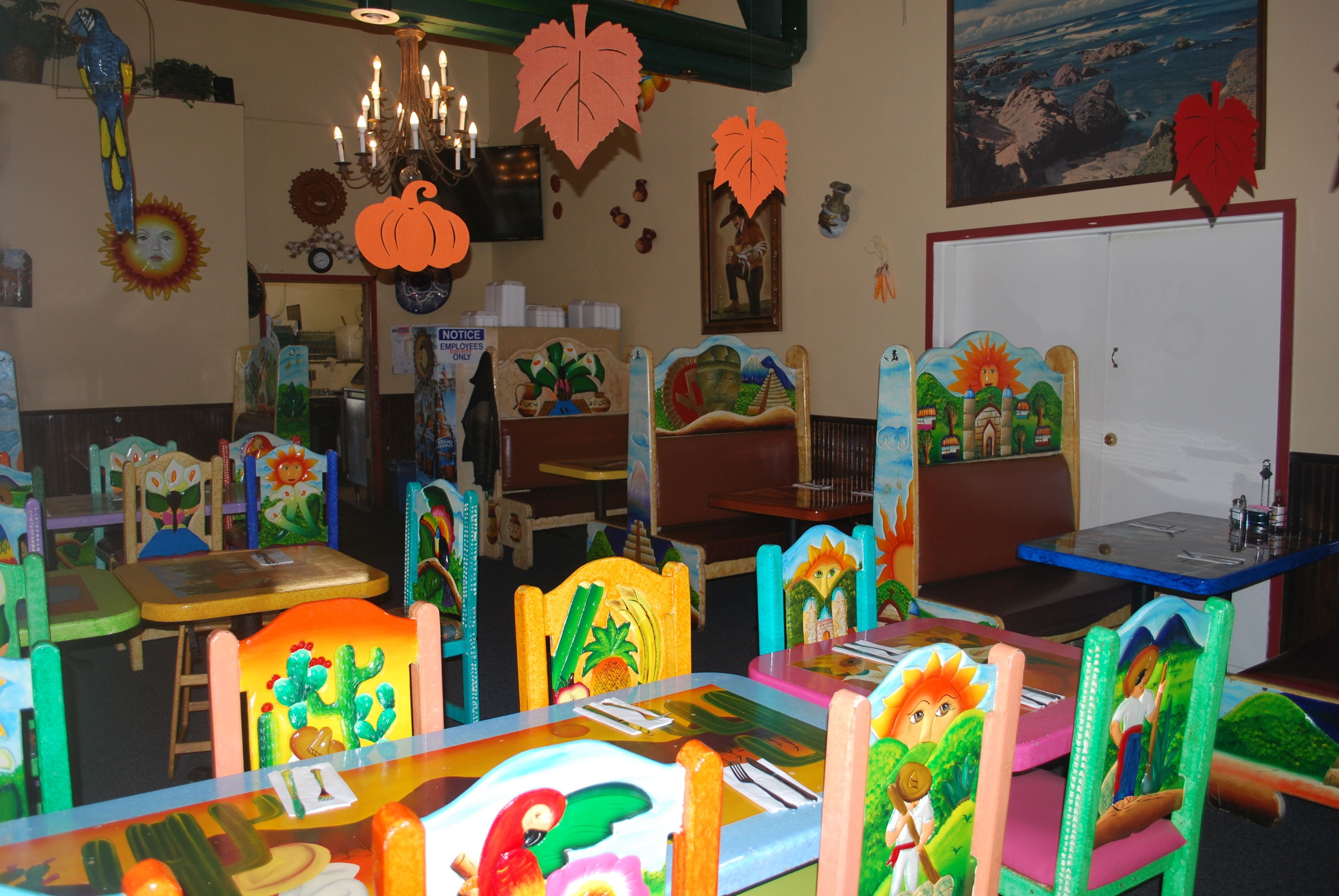 A restaurant with colorful, themed chairs and tables, a chandelier, and various wall decorations.