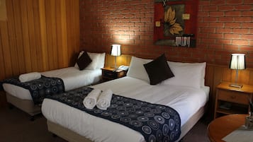 A hotel room with two beds, each with a patterned bedspread and pillows, a wooden headboard, a brick wall, and a painting above the beds.
