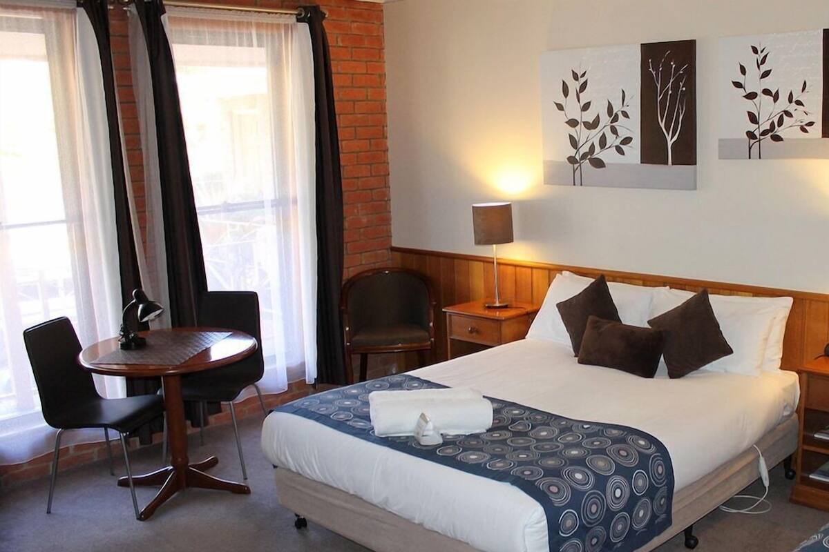 A hotel room with a bed, a desk, a chair, and a lamp.