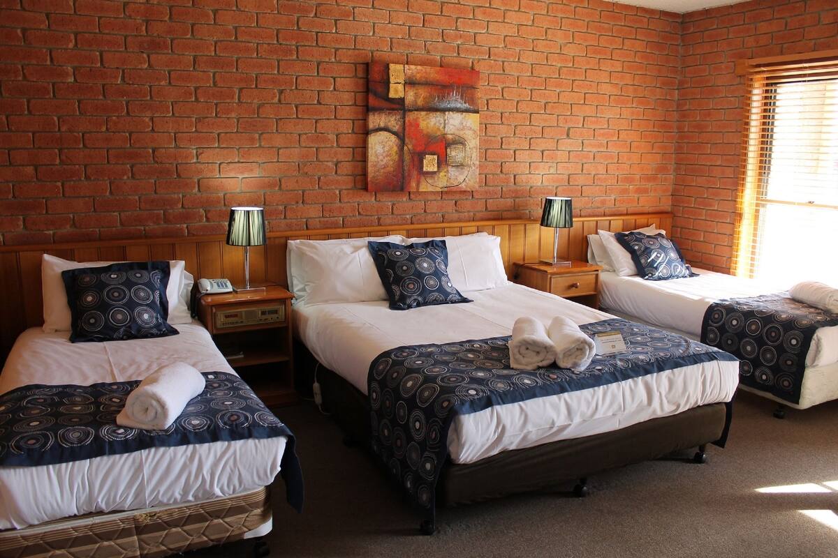 A hotel room with two beds, a brick wall, and a painting.