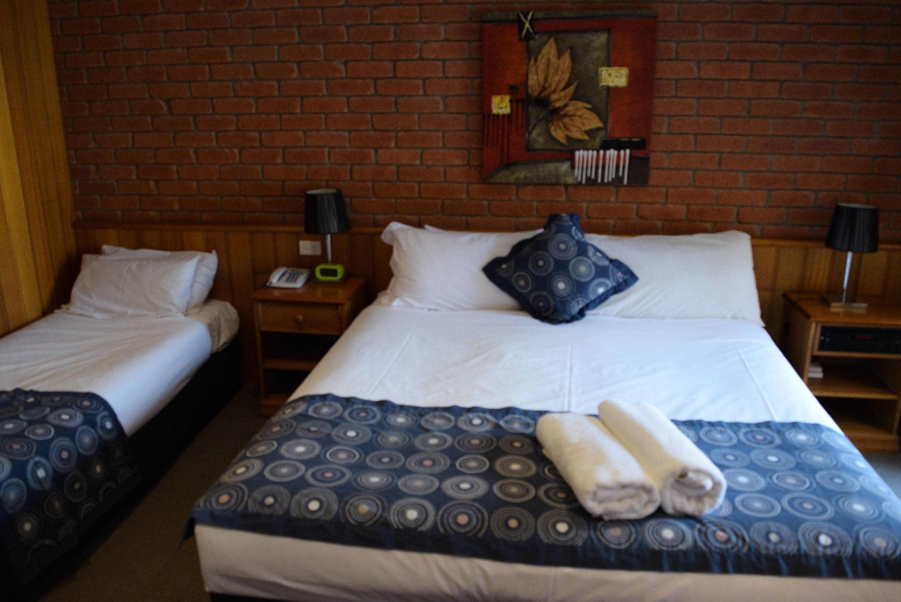 Hotellihuone, jossa on kaksi erillistä sänkyä, suuri sänky kuviollisella peitteellä ja tiiliseinä.