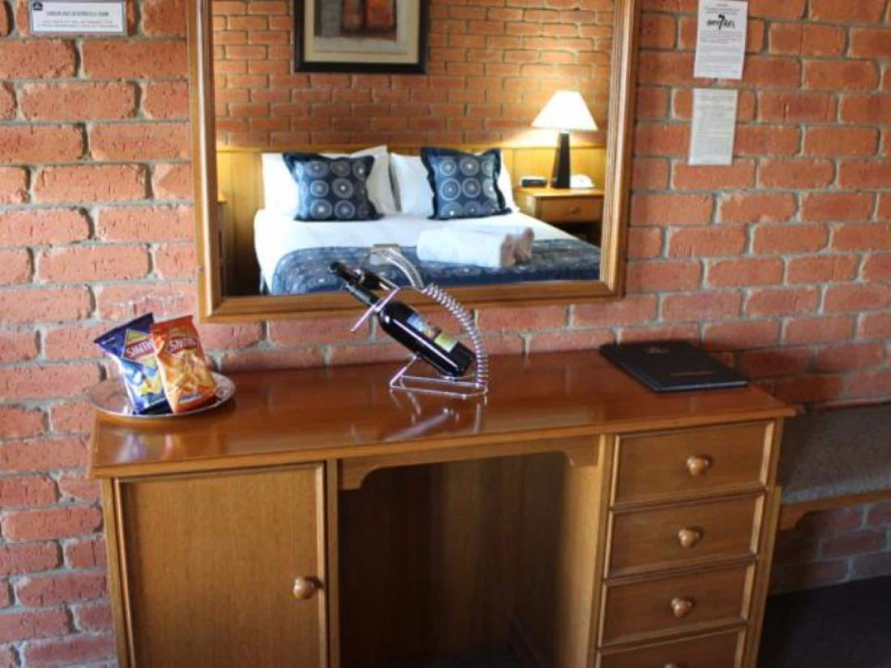 A wooden desk with a bottle of wine, a bag of chips, and a smartphone.