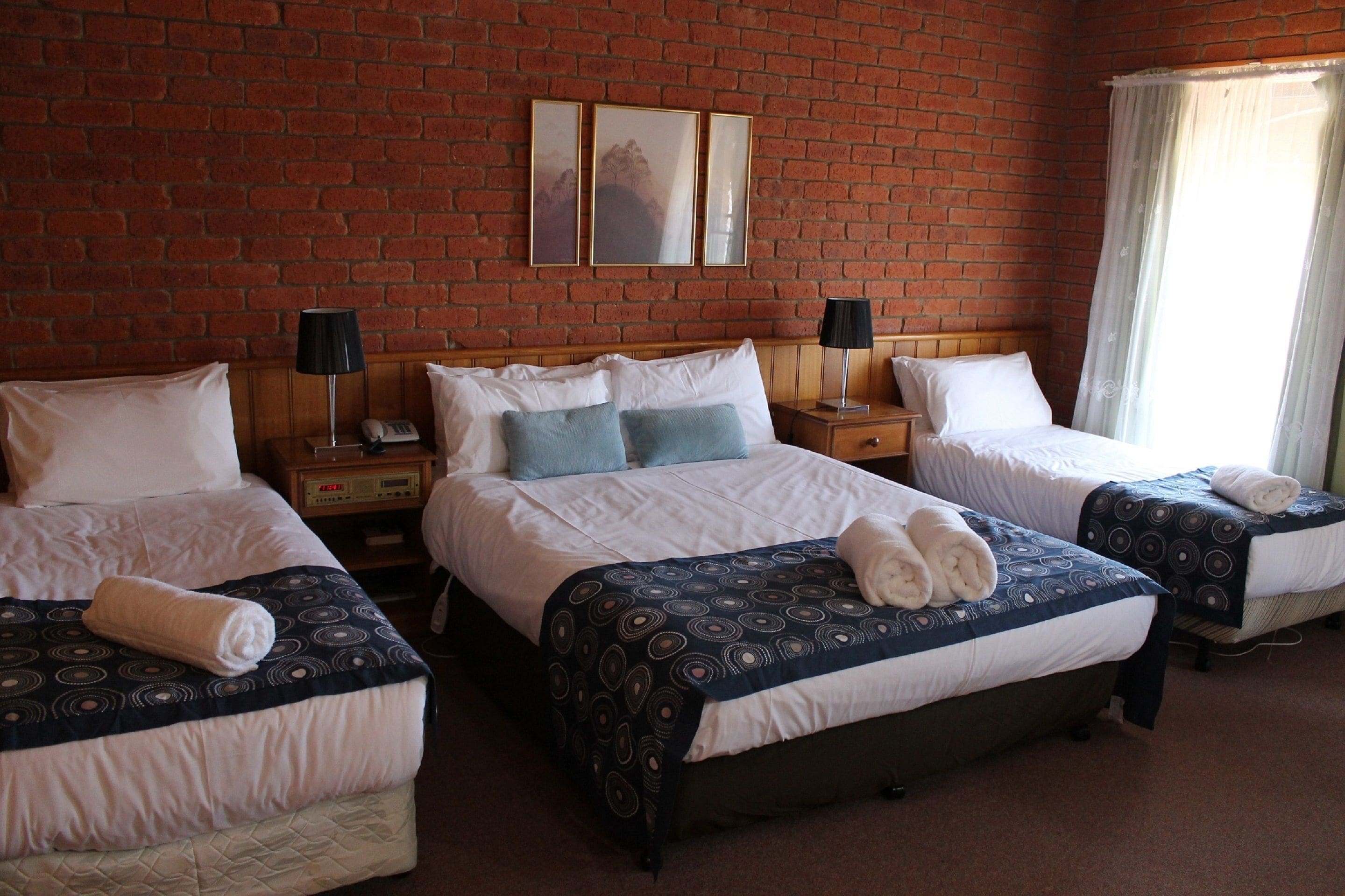 A hotel room with three beds, a brick wall, and a window with curtains.
