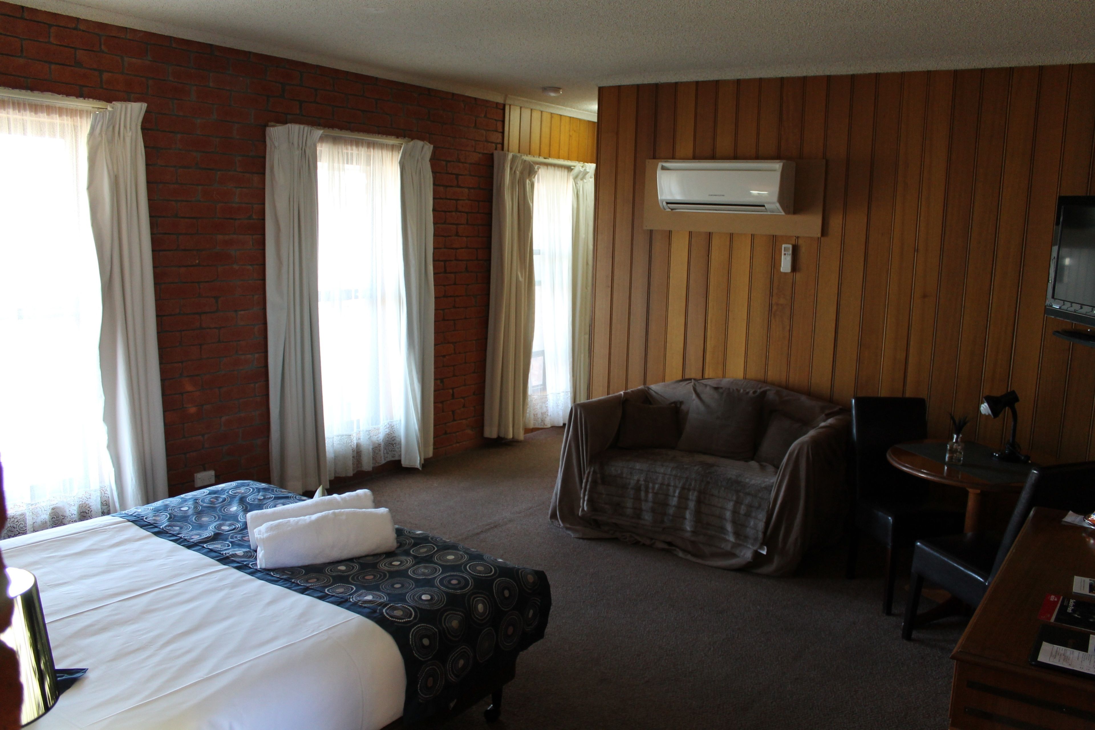 A hotel room with a large bed, a chair, a desk, and an air conditioning unit on the wall.