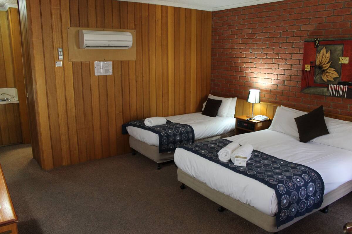 A hotel room with two beds, wooden paneling, a brick wall, and an air conditioning unit.