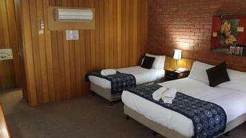 A hotel room with two beds, wooden paneling, a brick wall, and an air conditioning unit.