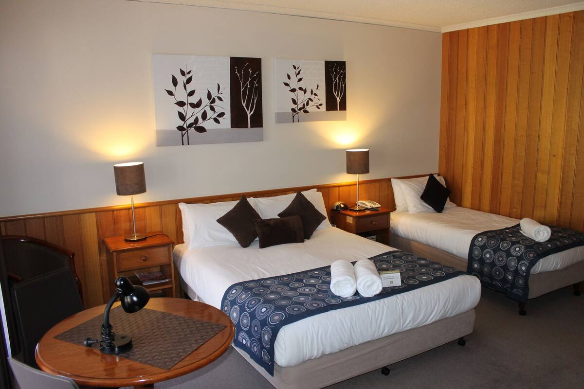 A hotel room with two beds, a desk, a chair, and a lamp.