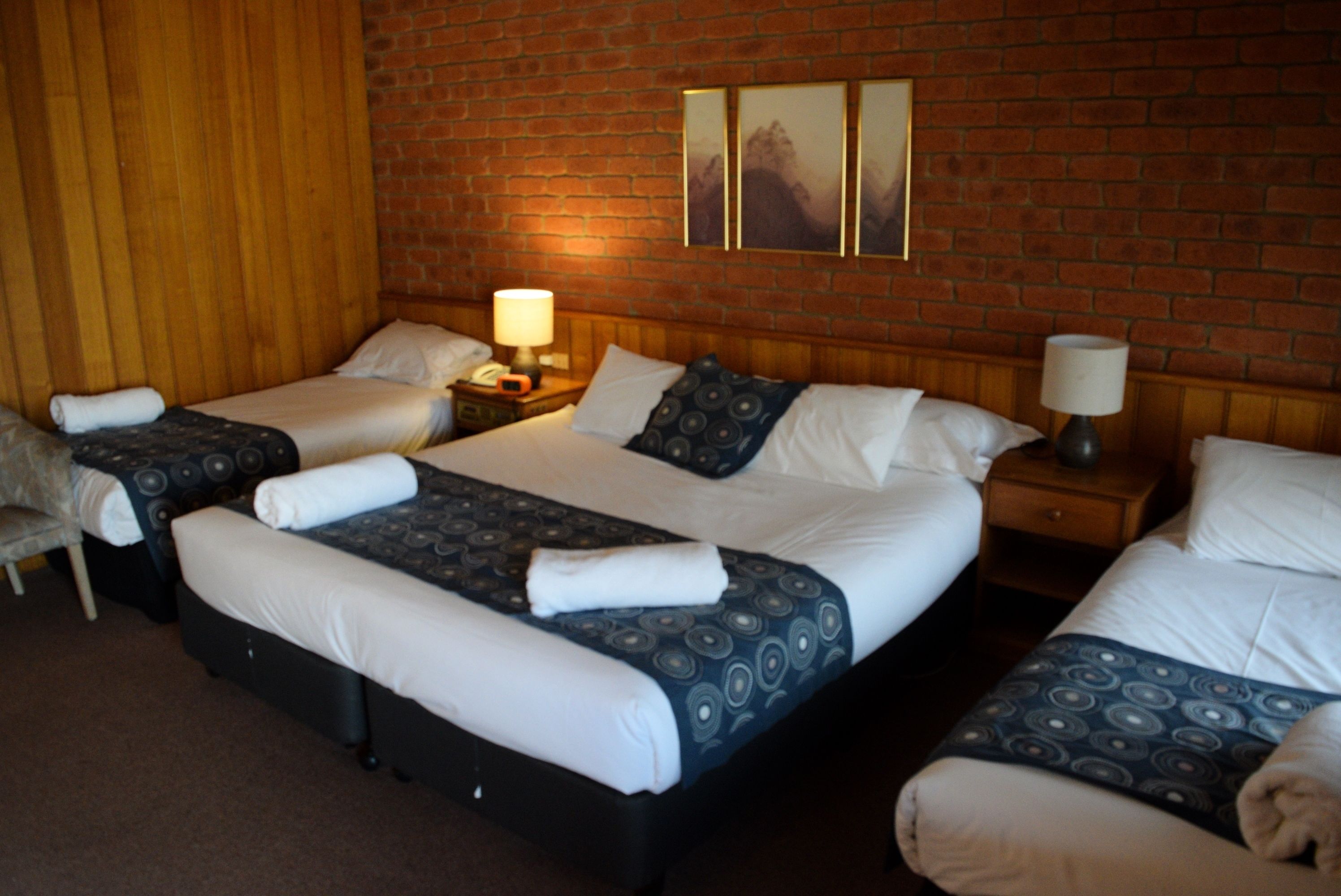 A hotel room with a large bed, two smaller beds, a wooden headboard, and a brick wall.