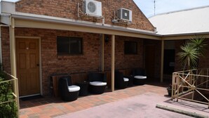 Edificio de ladrillo con patio cubierto, mobiliario exterior y unidades de aire acondicionado.