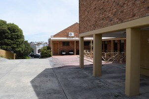 Un espacio al aire libre cubierto con un edificio de ladrillo al fondo, un patio de hormigón y una valla de madera.
