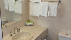 Un baño con lavamanos, espejo, toallero, inodoro y un cubo de basura.