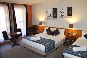A hotel room with a large bed, two bedside tables, a desk with a chair, and a window with curtains. - Bakery Hill Motel (Bakery Hill)