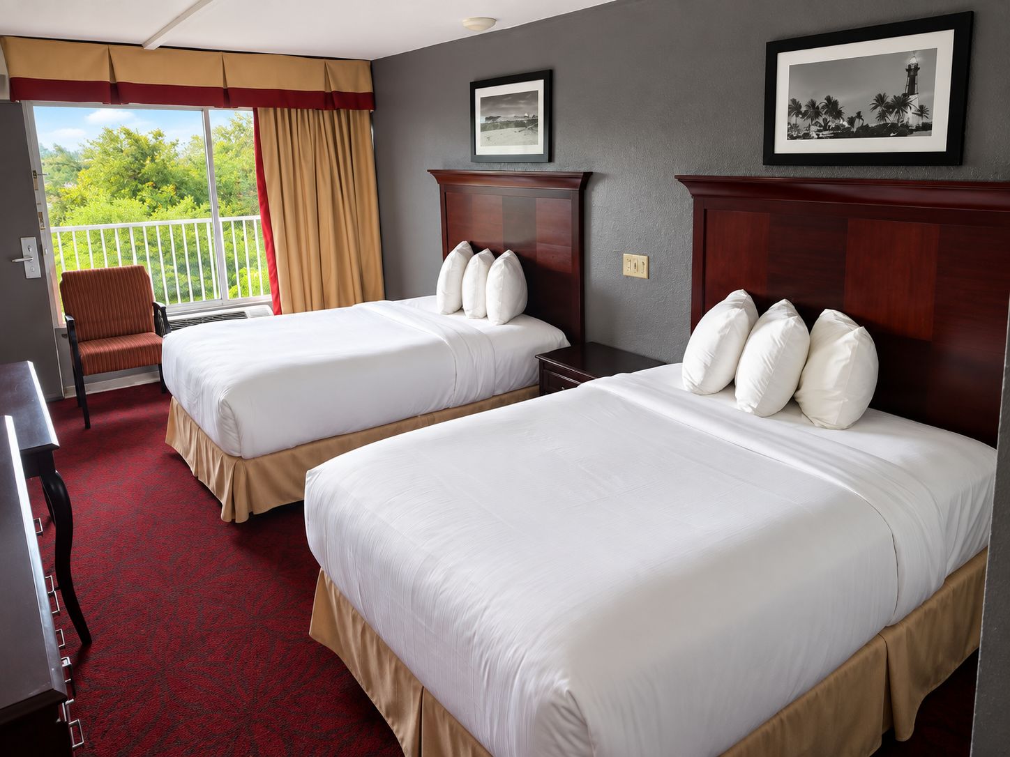 A hotel room with two beds, a chair, a desk, and a balcony with curtains.