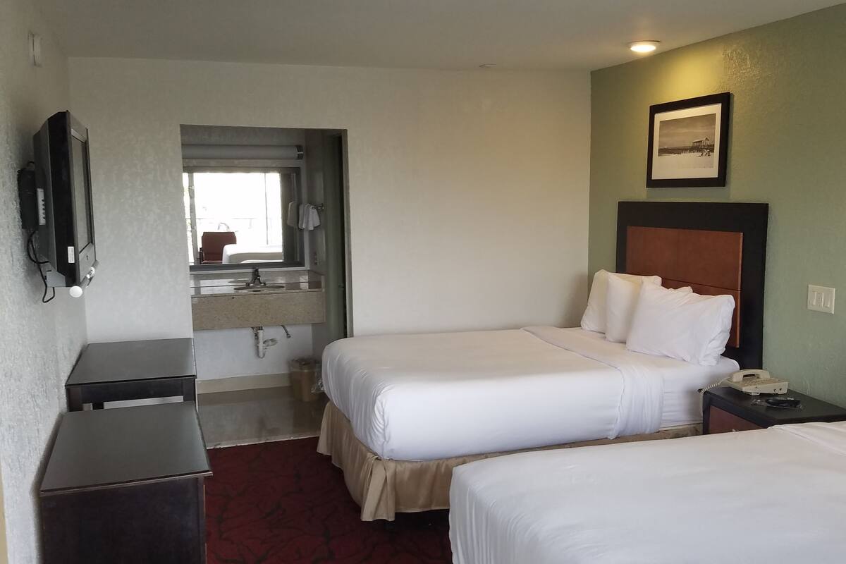 Ein Hotelzimmer mit zwei Betten, einem kleinen Schreibtisch, einem Spiegel, einem Fernseher und einem gerahmten Bild an der Wand.