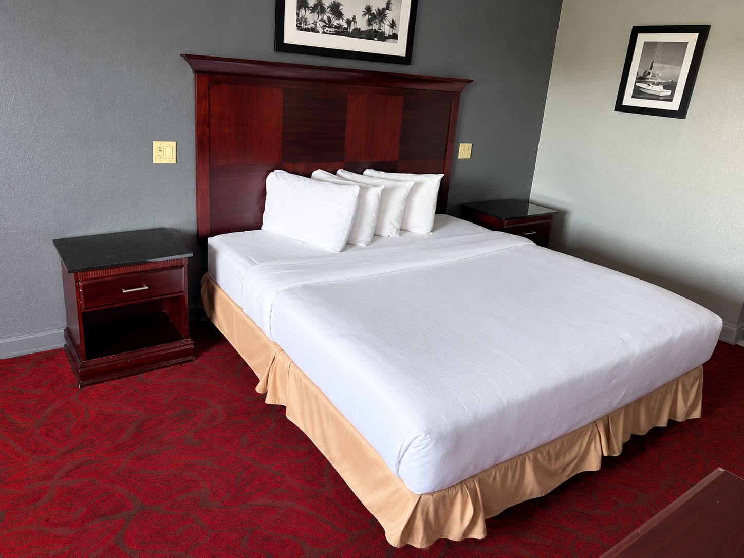 A hotel room with a large bed, two nightstands, a wooden headboard, and a red carpet.
