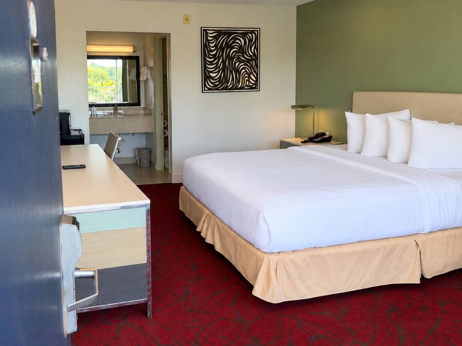 Een hotelkamer met een bed, een bureau, een stoel, een telefoon, een lamp en een kunstwerk aan de muur.