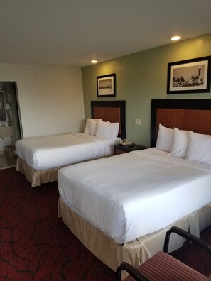 A hotel room with two beds, a small table, and a chair. - Budget Inn (Pompano Beach)
