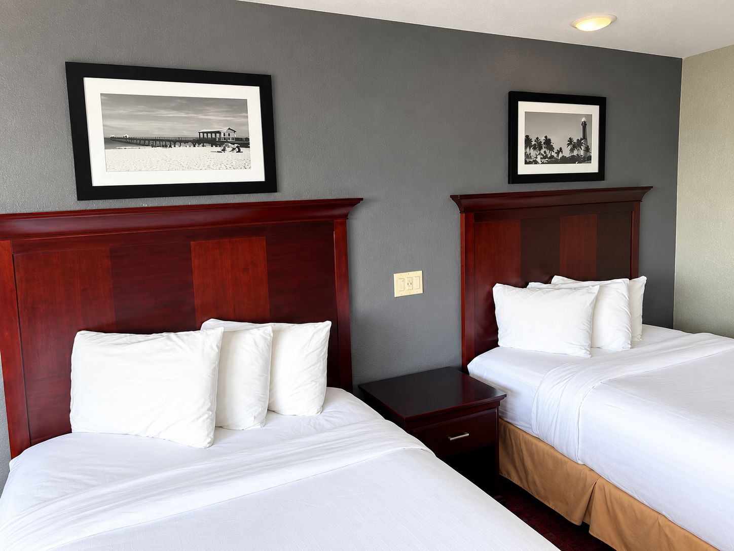 A hotel room with two beds, a nightstand, and two framed pictures on the wall.