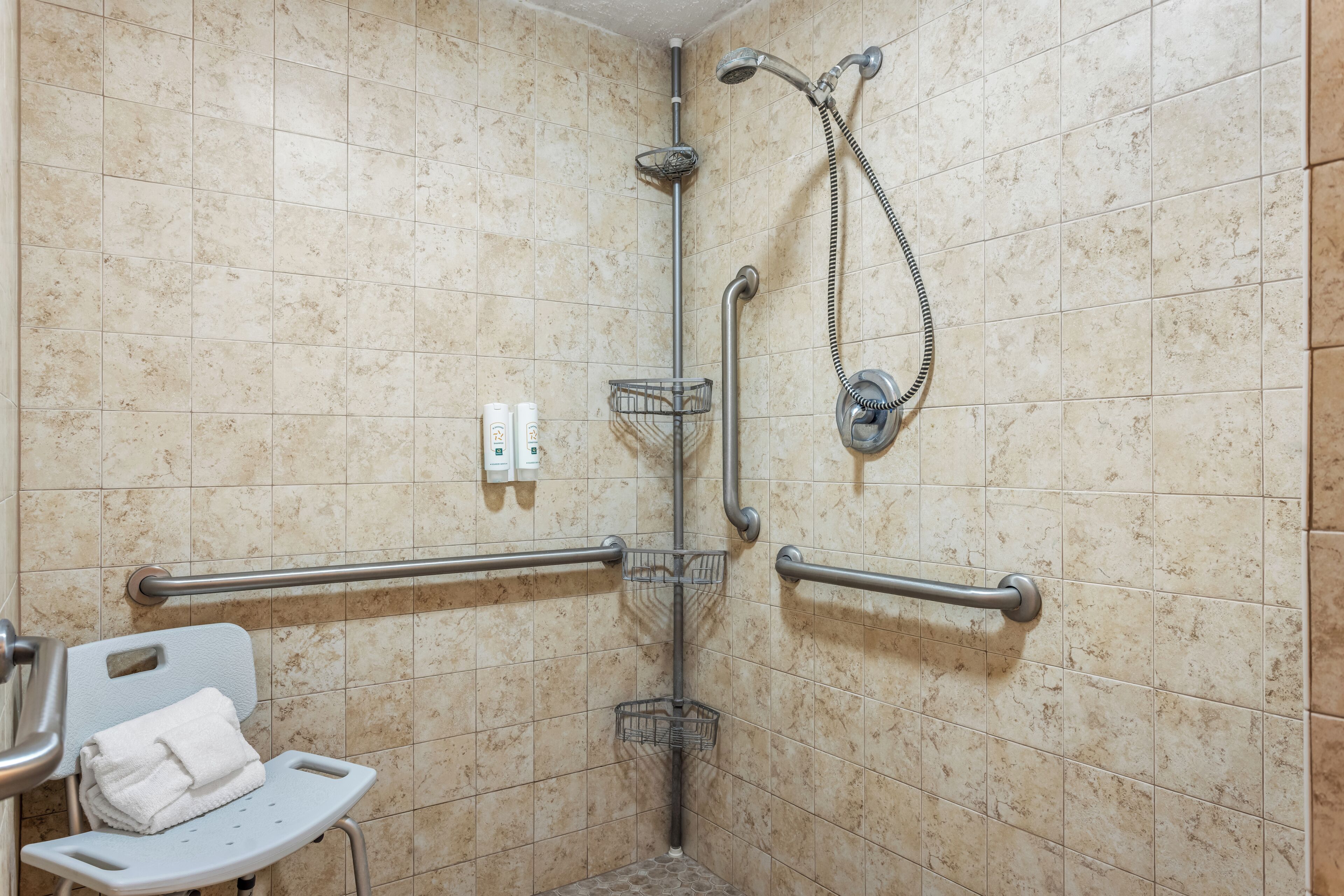 A shower area with grab bars, a towel rack, and a handheld showerhead.