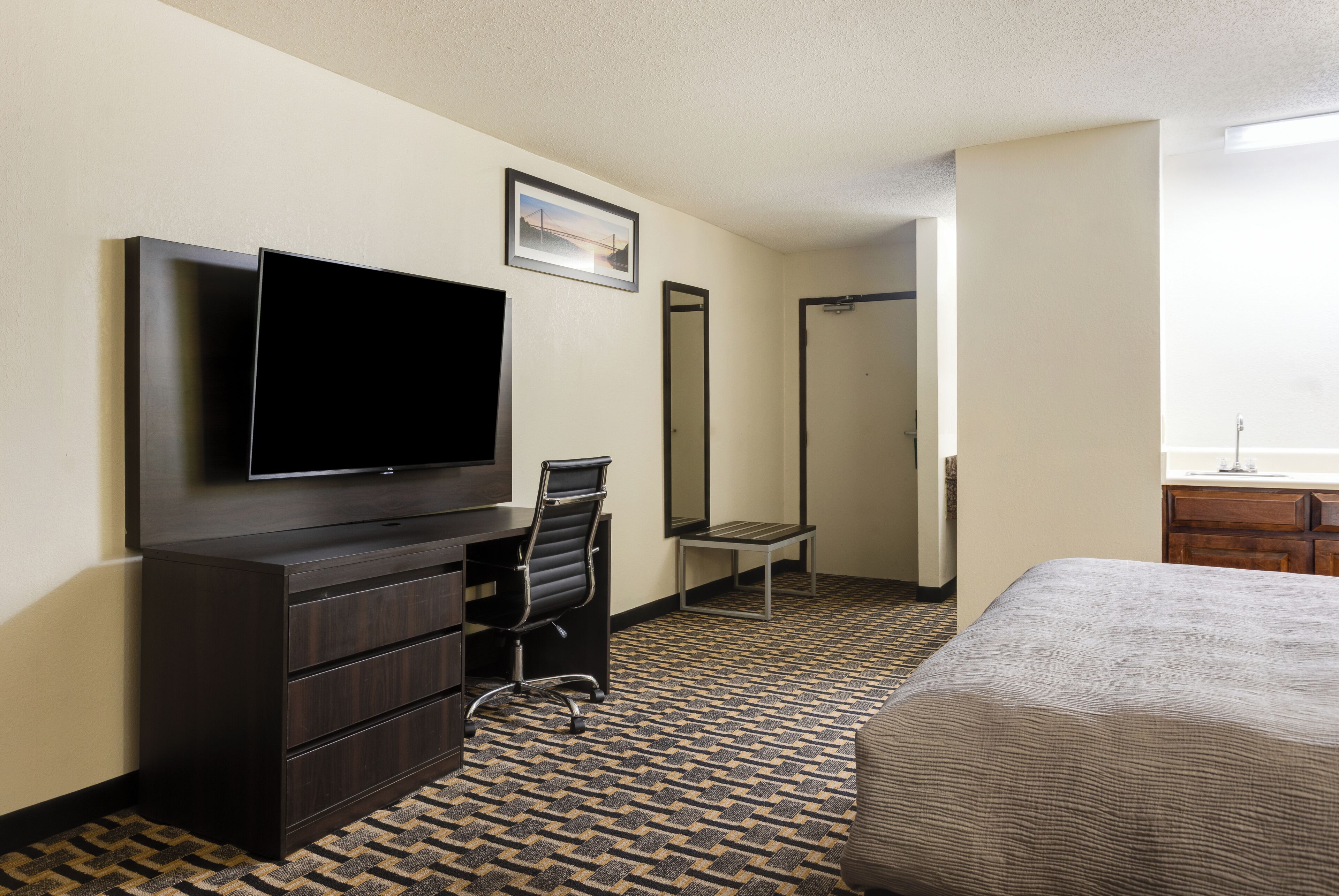 Hotelkamer met flatscreen televisie, bureau met stoel, bed, spiegel en een kamerbreed tapijt met dessin.