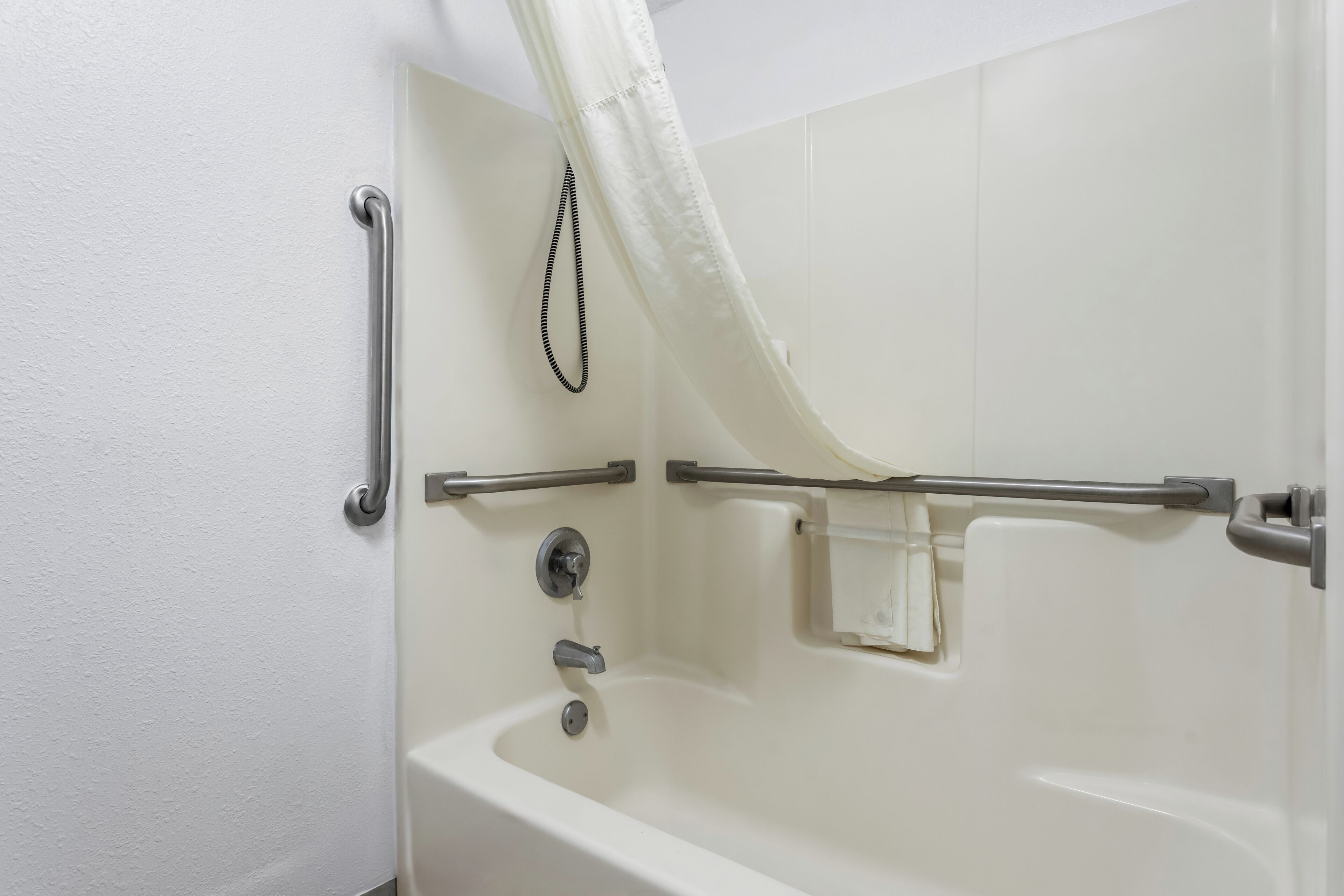 Un baño con bañera, barras de apoyo, cortina de ducha y cabezal de ducha manual.