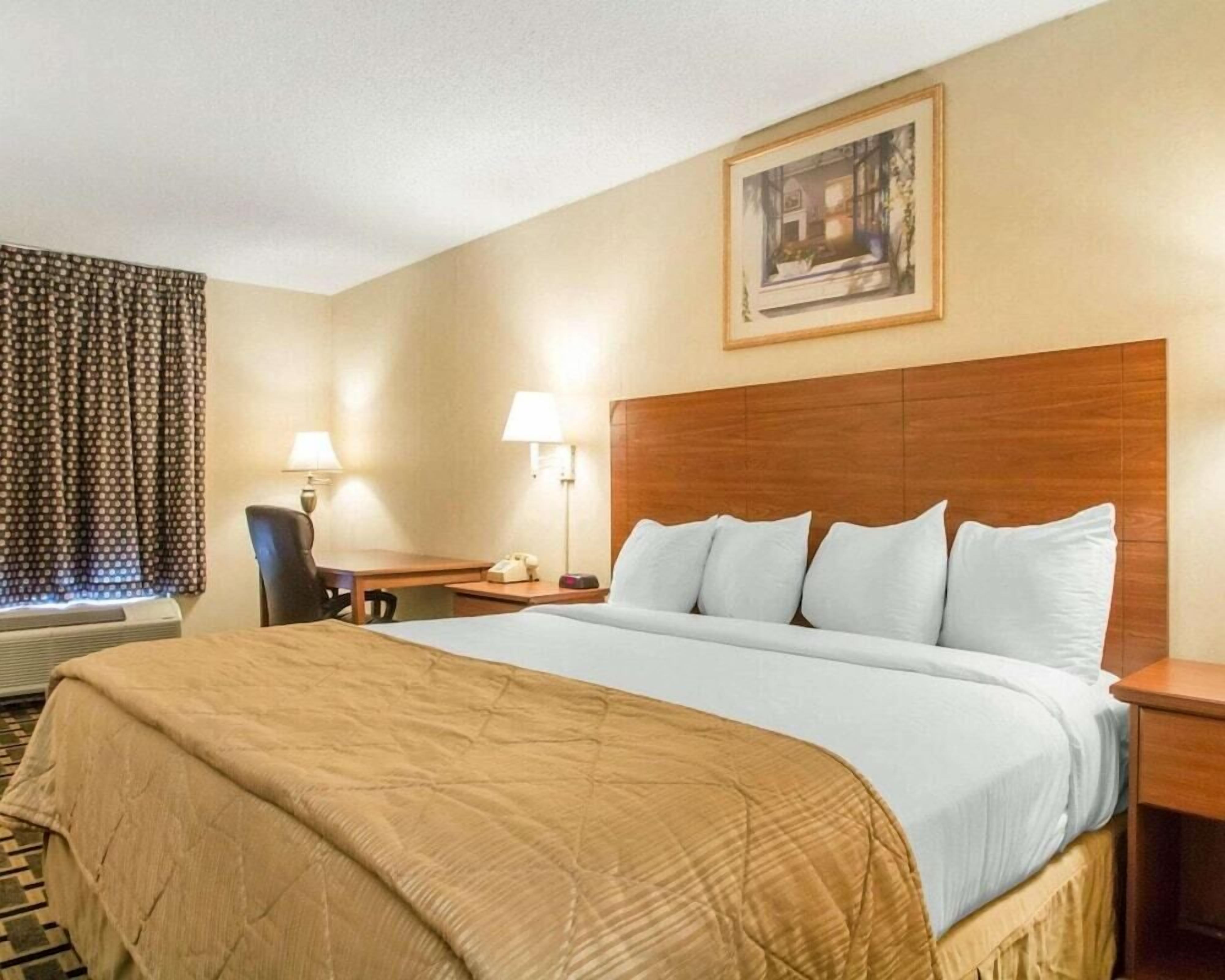 A hotel room with a large bed, a desk, a chair, and a window with curtains.