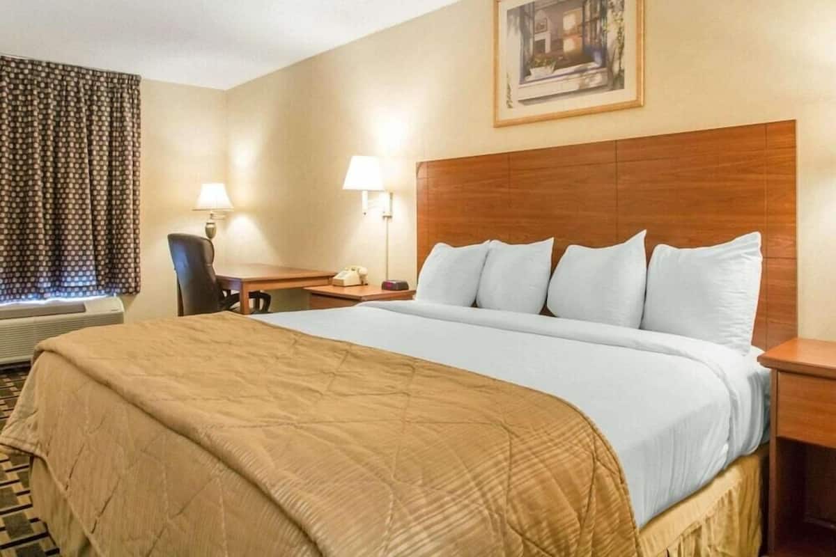 A hotel room with a large bed, a desk, a chair, and a window with curtains.
