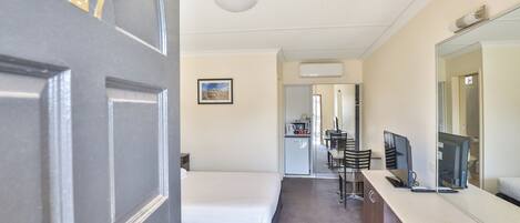 A hotel room with a bed, a desk with a computer, a mirror, and a door with a number.