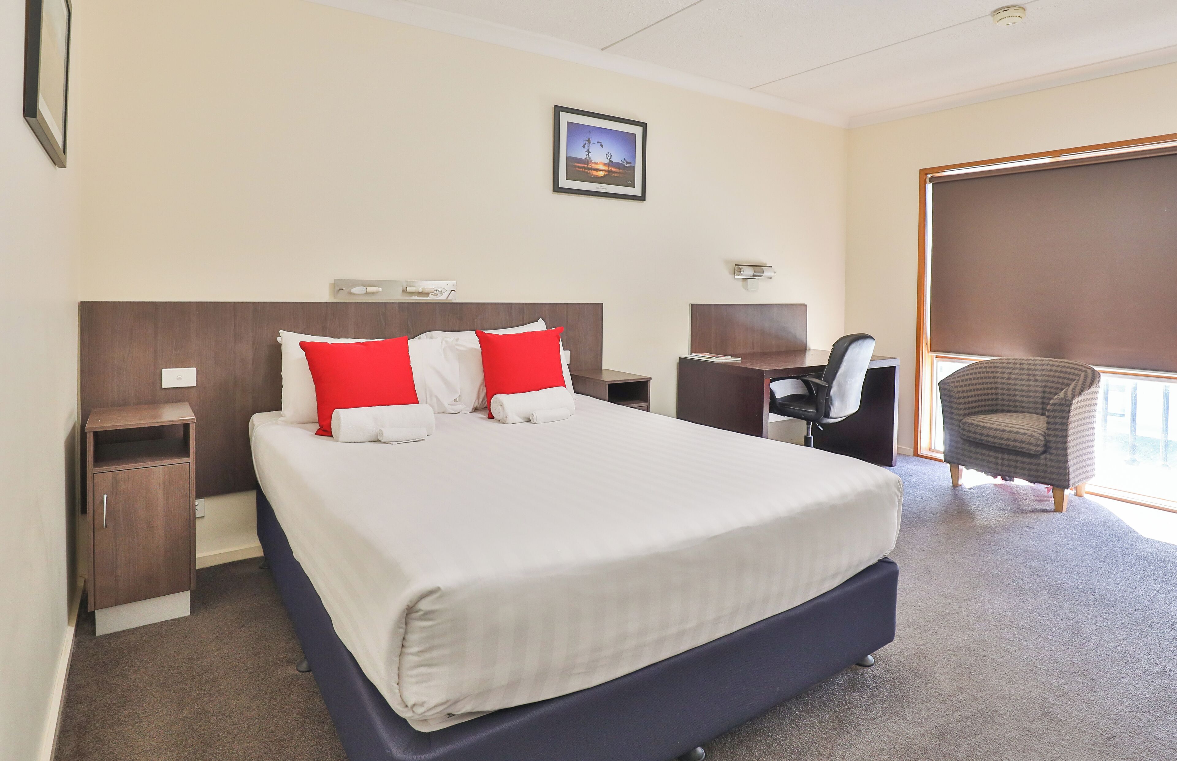 A hotel room with a large bed, two nightstands, a desk, a chair, and a window.