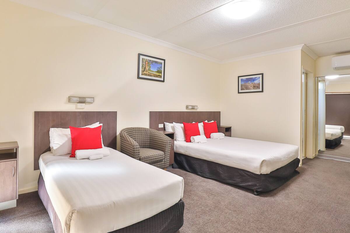Una habitación de hotel con dos camas, una silla y una mesita.