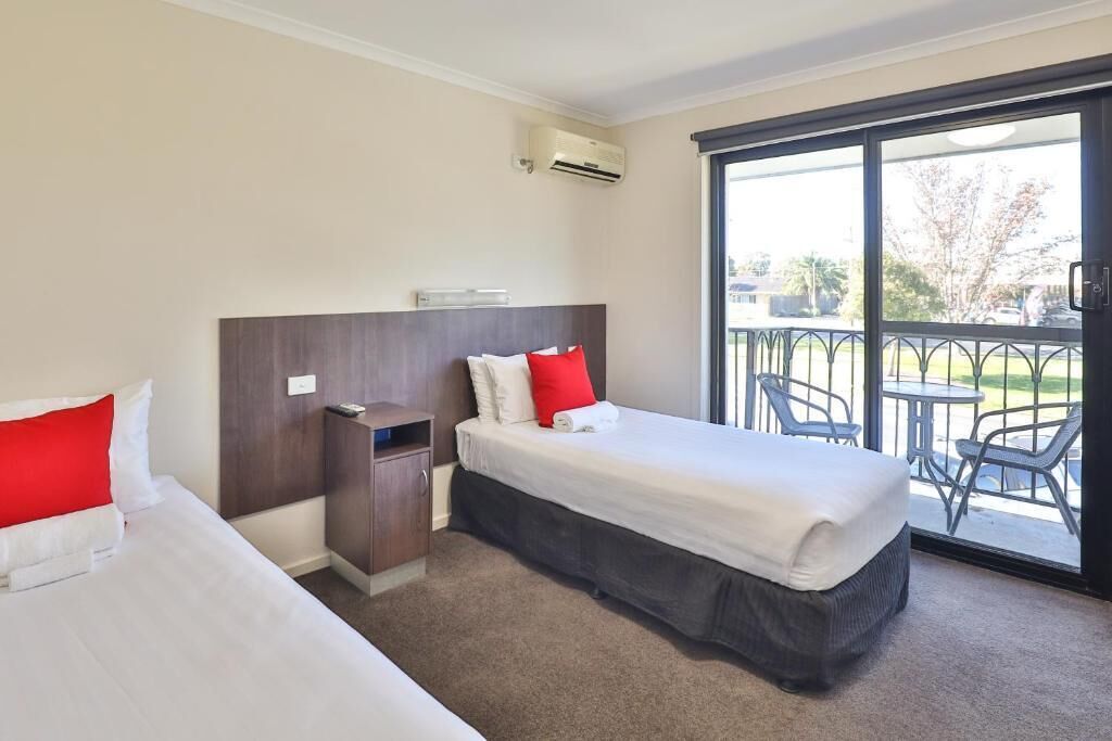 A hotel room with two beds, a balcony with outdoor seating, and an air conditioning unit.