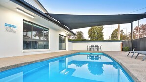 A swimming pool with a covered patio area, a pool rules sign, and a seating area with tables and chairs.