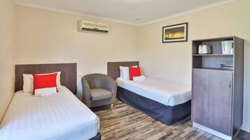 A hotel room with two single beds, a chair, a wardrobe, and a picture on the wall.