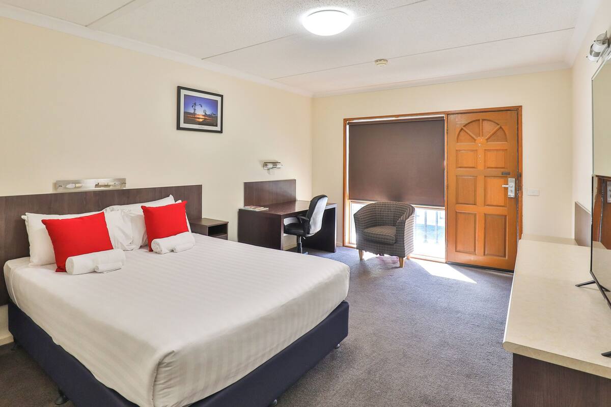 Una habitación de hotel con una cama grande, un escritorio, una silla y una puerta.