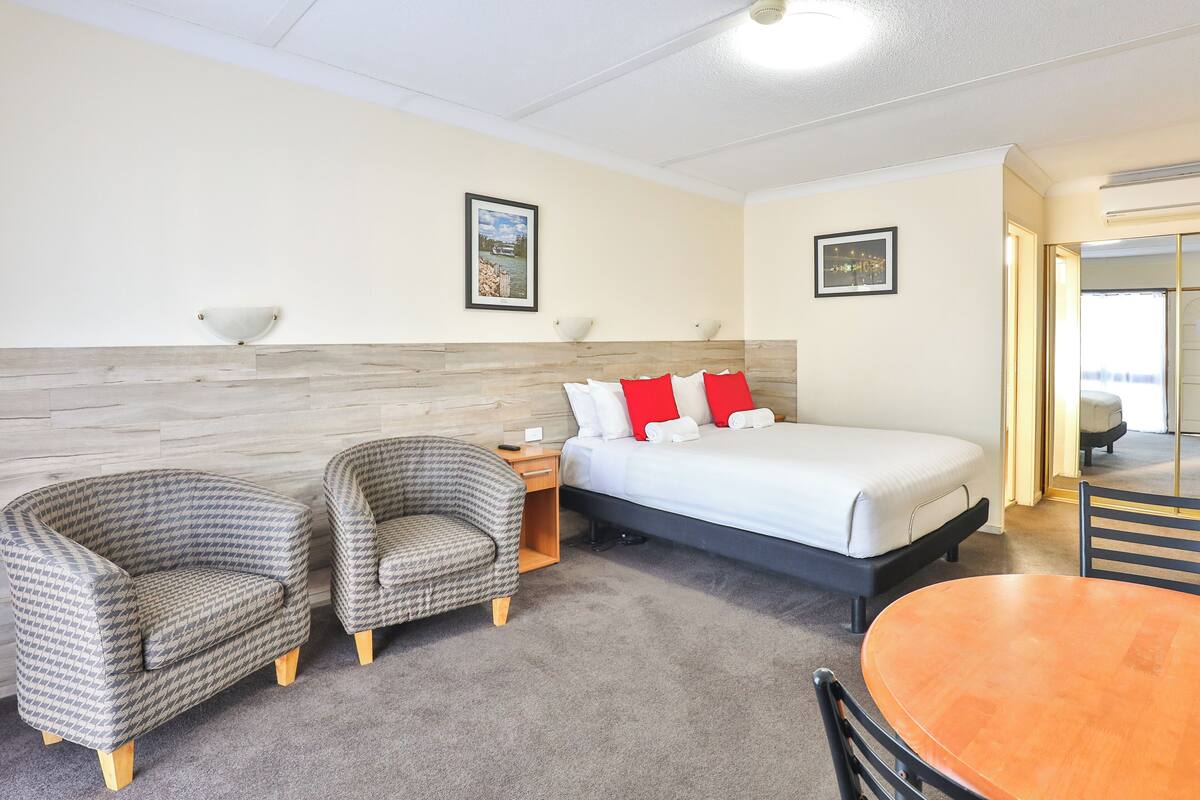 Habitación de hotel con una cama, dos sillones, una mesa de madera y vistas a la ciudad desde la ventana.