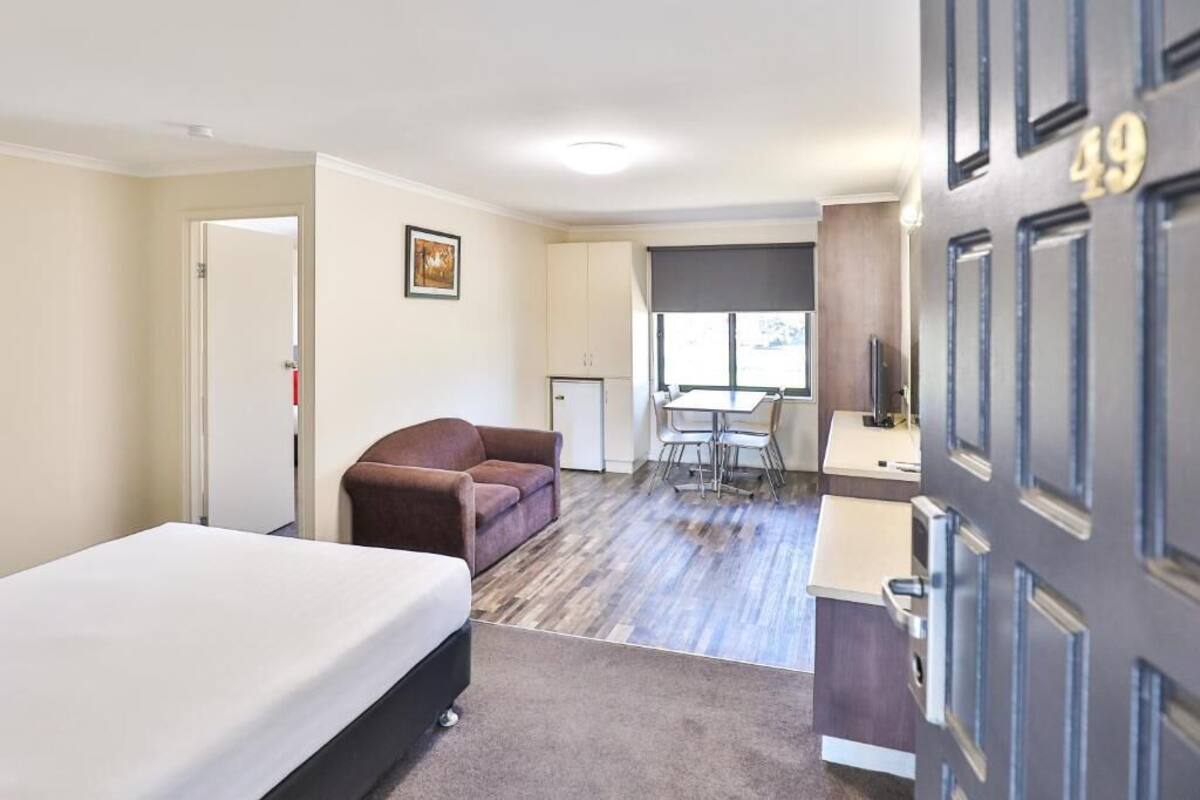 Habitación de hotel con cama, sofá marrón, mesa de comedor con sillas, pequeña cocina y una puerta con el número 49.