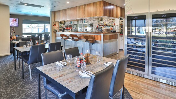 A restaurant with wooden tables, black chairs, and a bar area.