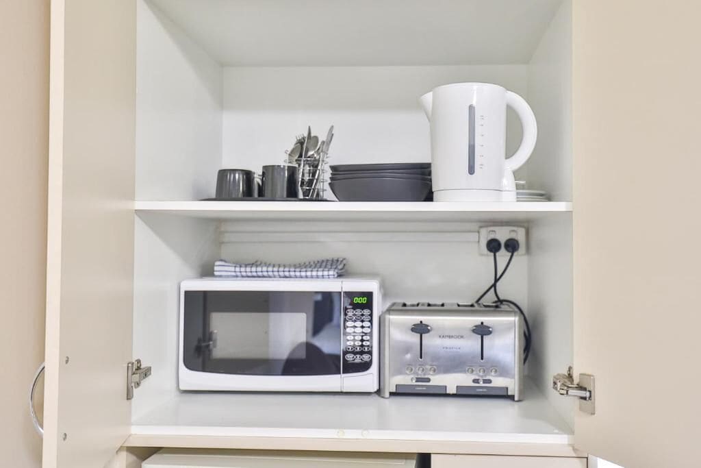 A kitchen with a microwave, toaster, and a coffee maker on the shelf.