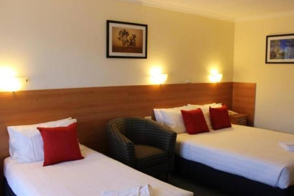 Una habitación de hotel con dos camas, una silla y lámparas fijadas a la pared.