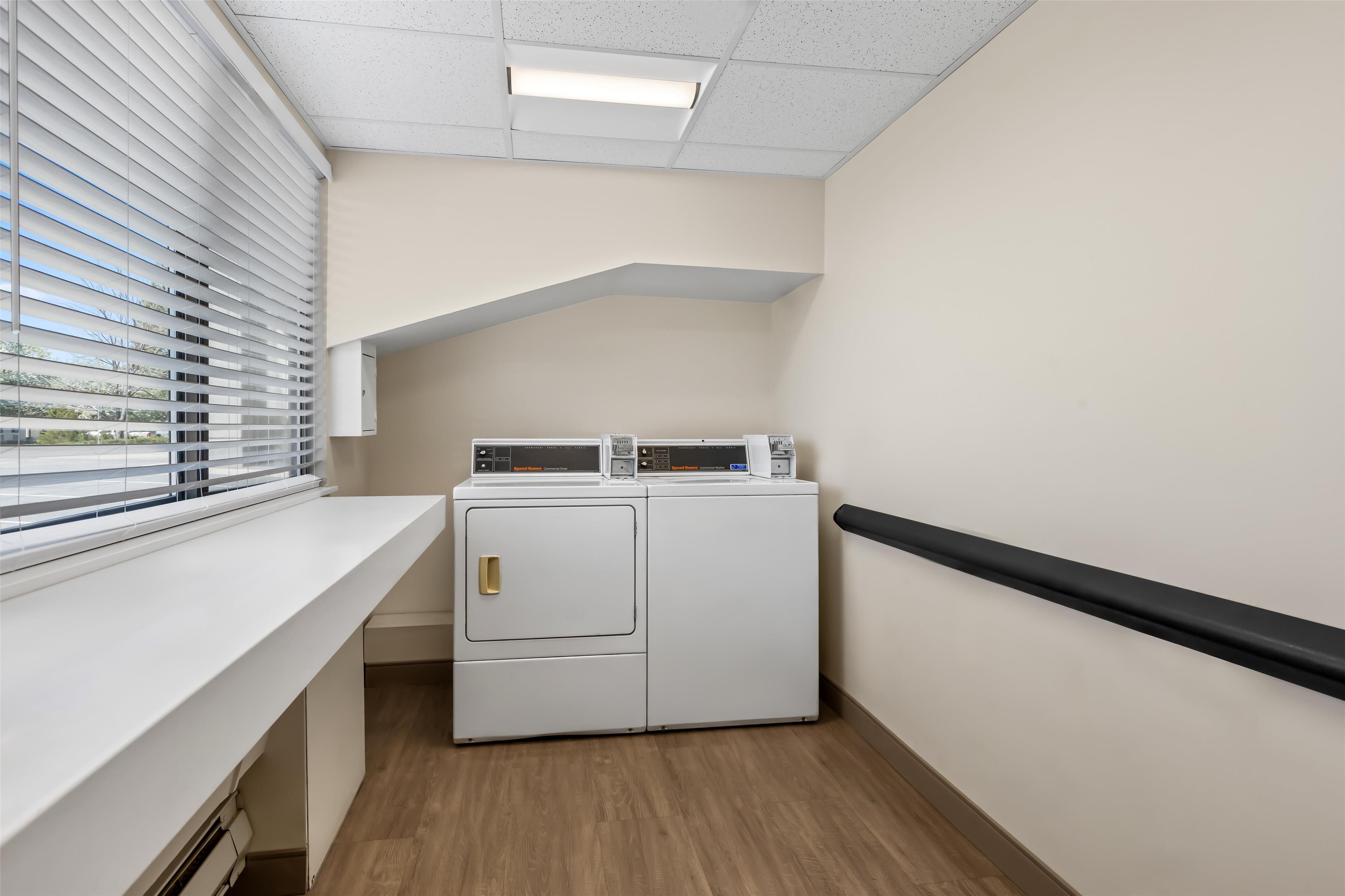 A laundry room with a washing machine and dryer, a window with blinds, and a white countertop.