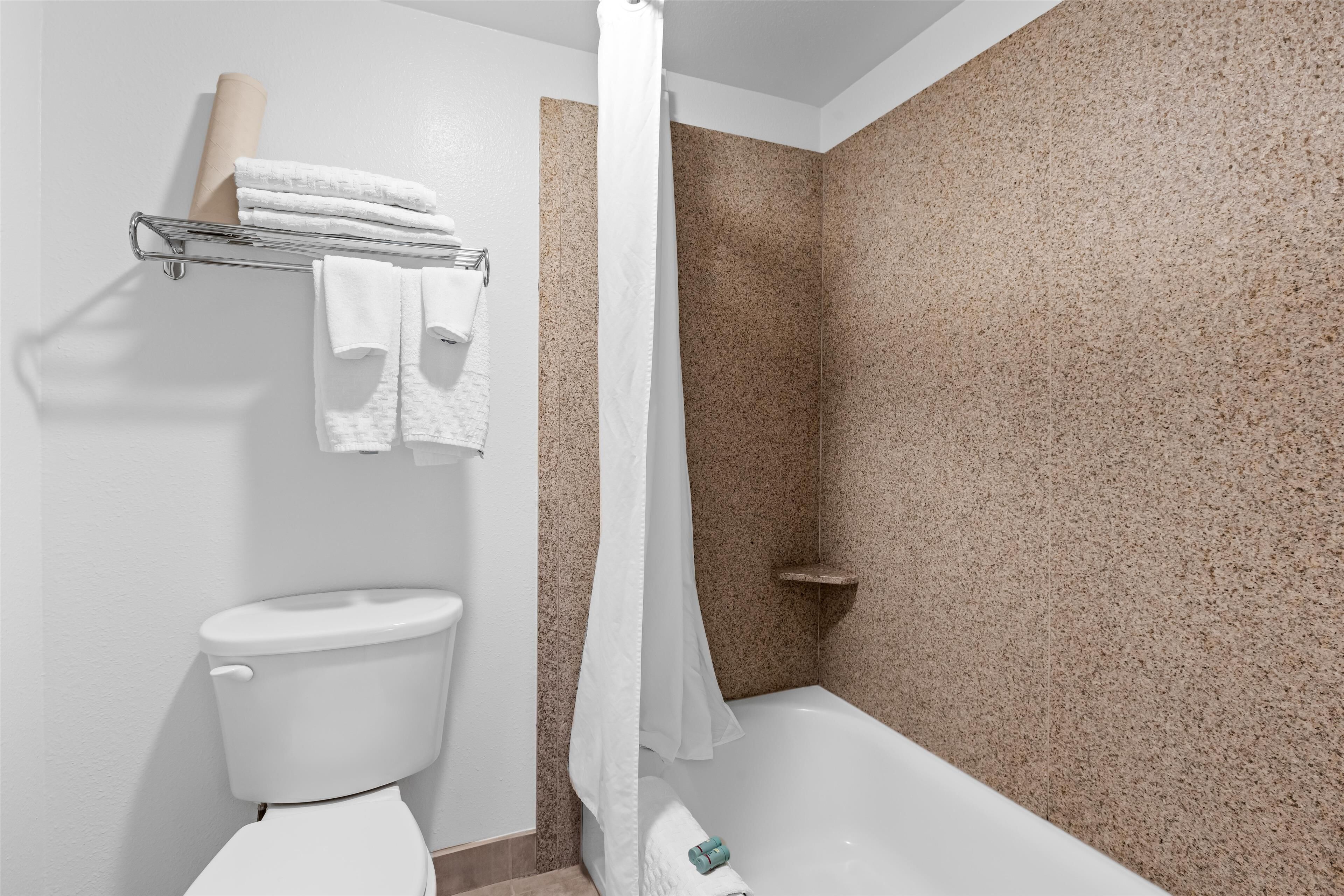 Et badeværelse med toilet, bruser med gardin og et håndklædestativ med foldede håndklæder.
