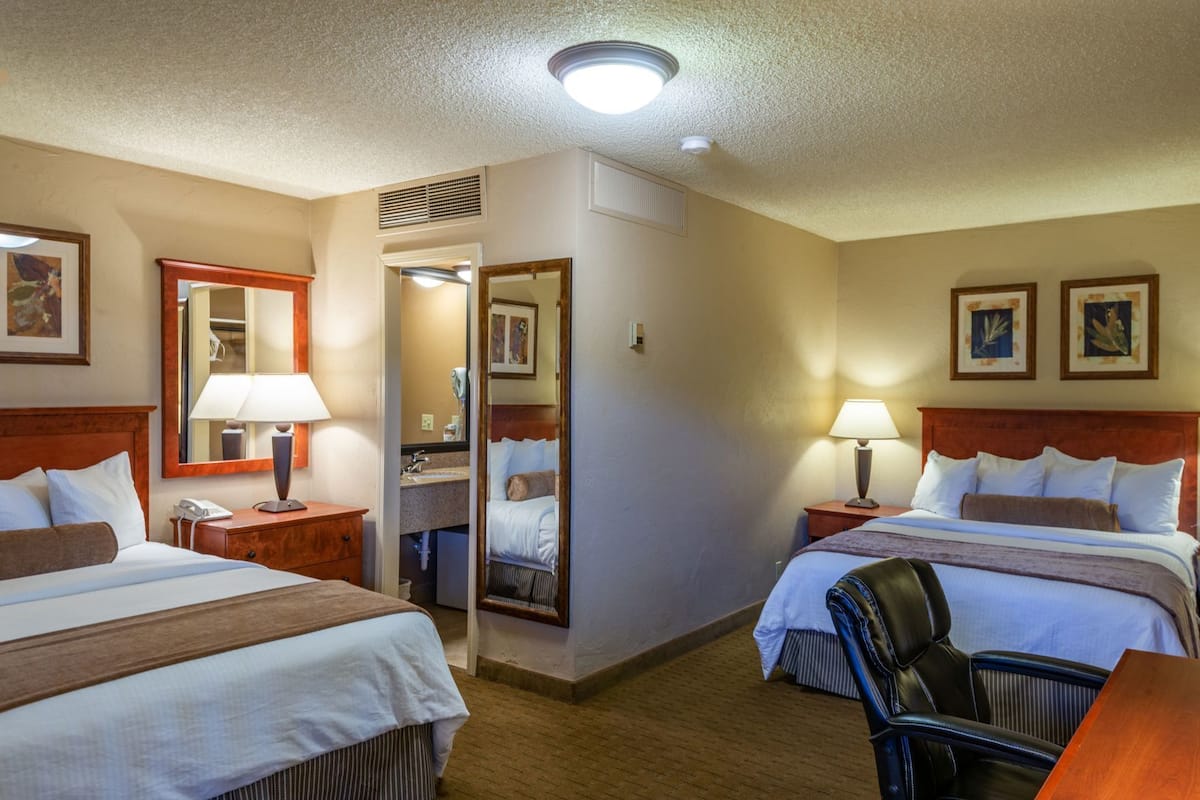 Ein Hotelzimmer mit zwei Betten, einem Schreibtisch, einem Stuhl, einem Badezimmer und einem Spiegel.