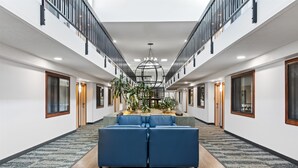A spacious hotel lobby with a central seating area, a staircase, and a large chandelier.